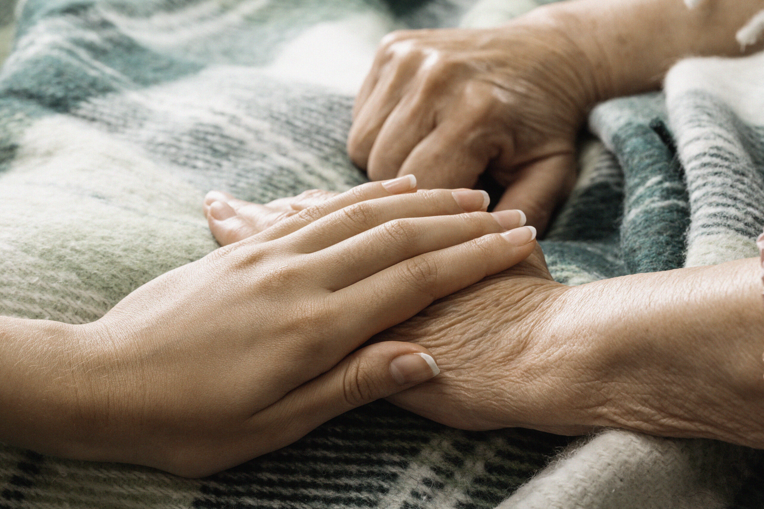 Die Hand einer jungen Frau berührt und hält die Hand einer alten Dame